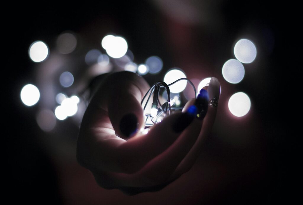 Close-up of a hand holding glowing string lights with a bokeh effect, creating a festive atmosphere.