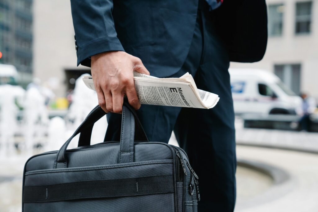 Close-up of businessman in suit holding a briefcase and newspaper in urban setting.