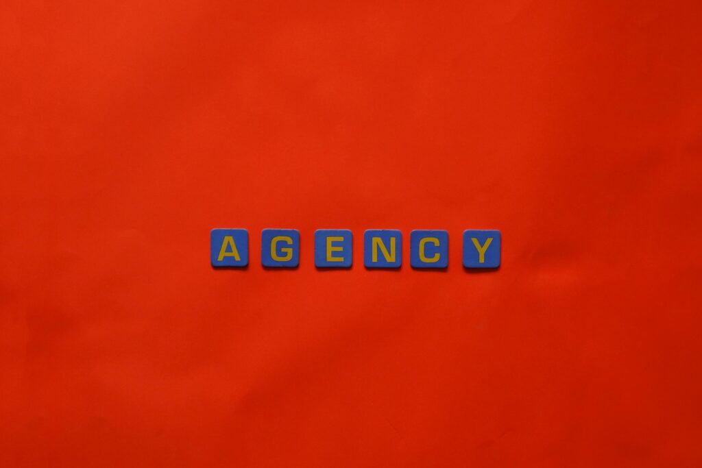 Blue letter tiles spelling 'AGENCY' on a vibrant red background, ideal for creative promotion.